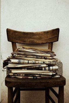 a wooden chair sitting next to a stack of newspapers