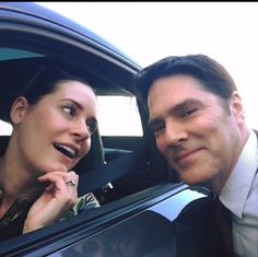 a man and woman sitting in the back seat of a car, smiling at the camera