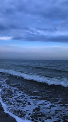 the ocean with waves coming in to shore and dark blue sky above, on an overcast day