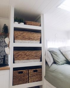 a bed with baskets on top of it next to a shelf filled with blankets and pillows