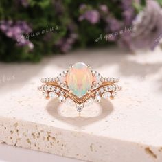 an opal and diamond ring sits on top of a piece of white rock with purple flowers in the background