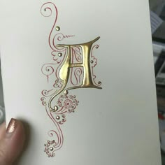 a person holding up a card with the letter h on it in gold and red