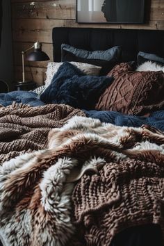 an unmade bed with blankets and pillows on top of it in front of a wooden wall