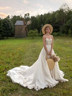 a woman in a white dress and straw hat standing on the grass holding a basket