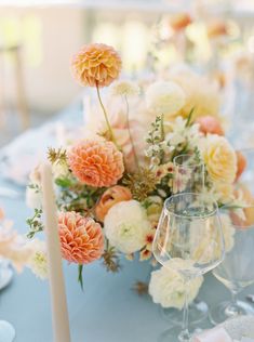 an arrangement of flowers on a table with wine glasses and place settings in front of it