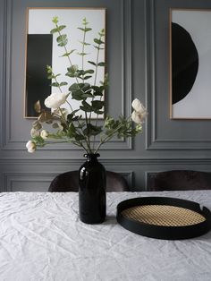 a black vase with white flowers in it on a table next to a round tray