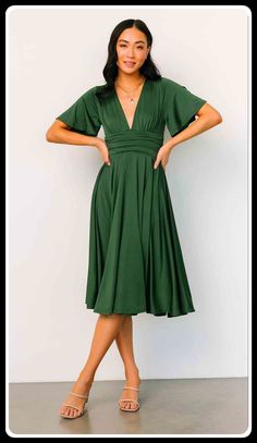 a woman in a green dress standing with her hands on her hips and looking at the camera