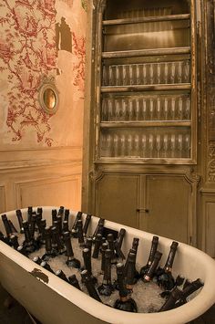 a bath tub filled with lots of empty wine glasses in front of a book shelf