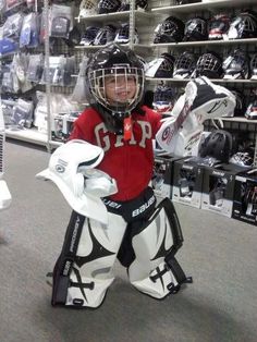 a young boy dressed as a hockey goalie holding his helmet and gloves in a store