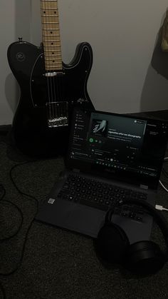 a laptop computer sitting on top of a desk next to a guitar and headphones