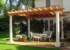 an outdoor patio with table and chairs under a pergolated arbor in front of a house