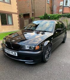 a black bmw is parked in front of a brick building on the side of the road