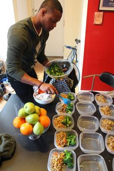 a man preparing food on top of a table next to fruit and vegetables in plastic containers