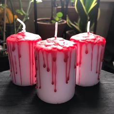 three candles with red and white drips on them sitting on a table next to potted plants