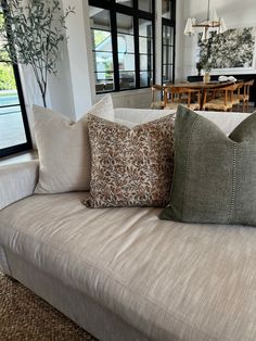 a couch with two pillows on it in front of a dining room table and windows