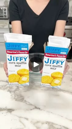 a woman holding two boxes of jiffy corn chips on top of a kitchen counter