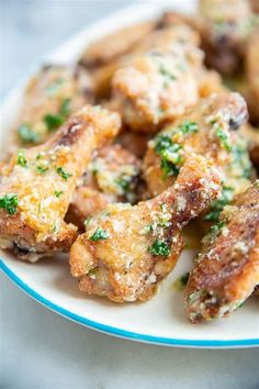 a white plate topped with chicken wings covered in parmesan cheese and seasoning