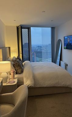 a bedroom with a large bed and two chairs in front of a window overlooking the city