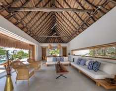 a living room with white couches and wooden tables in front of a thatched roof