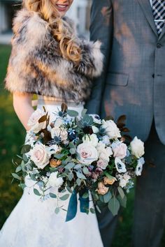 a bride and groom standing in front of a house with their bouquets on the grass