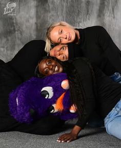 three women posing for a photo with a purple monster stuffed animal in front of them