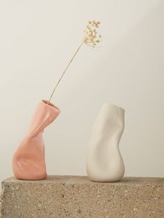 two ceramic vases sitting on top of a stone slab with a flower sticking out of one