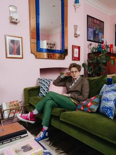 a woman sitting on top of a green couch in a living room next to a mirror