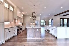 a large kitchen with white cabinets and an island in the middle of it is lit by pendant lights