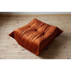 an orange square cushion sitting on top of a wooden floor