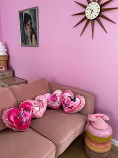 a living room with pink walls and decorative items on the couch, in front of a clock