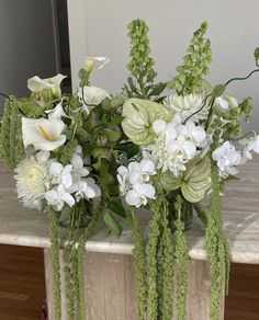 white flowers and greenery in a vase on a marble table with a mirror behind them