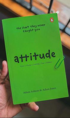 a person holding up a green book with the words attitude written on it