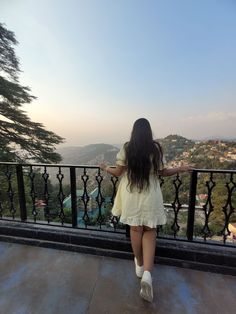 a woman standing on top of a balcony next to a tree filled hillside with houses in the distance