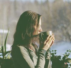 a woman drinking from a coffee cup in front of a window with snow on the ground