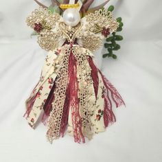 an angel made out of fabric and lace on a white surface with flowers in the background