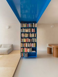 a blue book shelf filled with lots of books next to a white couch and table