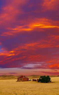 an orange and purple sunset over a farm house in the middle of nowhere, with red clouds