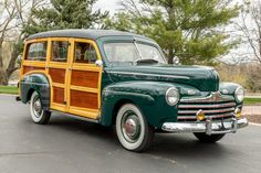 an old green and wood car is parked in the street