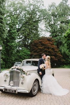 a bride and groom standing next to an old car