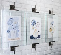 three glass frames are hanging on a brick wall with flowers in vases behind them