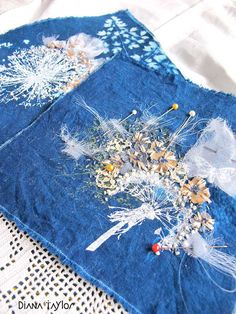 two pieces of blue fabric with white flowers and feathers on them sitting on a doily