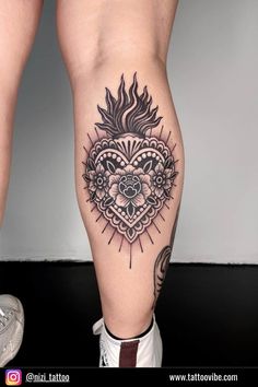 a woman's leg with tattoos on it and an ornate heart in the middle