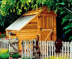 a small wooden shed with a white picket fence and flowers in the yard next to it