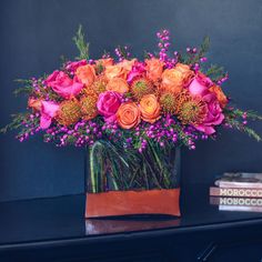 a vase filled with orange and pink flowers on top of a black table next to books