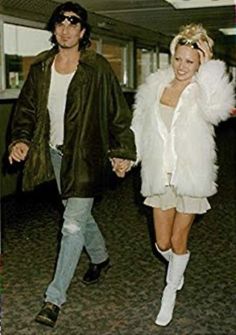 a man and woman walking through an airport holding hands, both wearing white fur coats