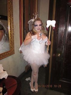 a woman dressed up as a fairy holding a wand and wearing a white tutu while standing in front of a mirror