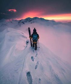 a person with skis on top of a snow covered mountain at sunset or dawn