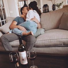 a man and woman sitting on a couch with wine glasses in front of them, kissing