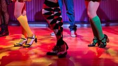 three women in brightly colored stockings and high heeled shoes are standing on a stage