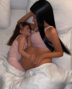 two women laying in bed with one holding the other's stomach and touching her breast